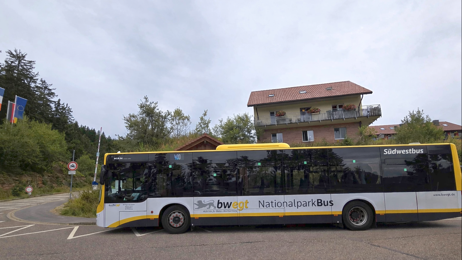 Bwegt Bus gelb, weiss, schwarz bei einer Bushaltestellte mit einem Gebäude im Hintergrund