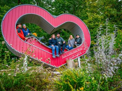 Wanderer sitzen im roten Aussichtsherz bei Waldulm und blicken über das Tal