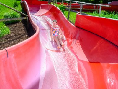 Kind auf einer roten Rutsche im Schwimmbad