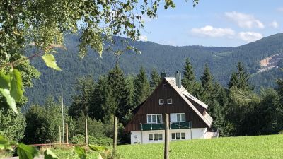 Braun, weißes Haus auf einer Wiese mit Bergen im Hintergrund
