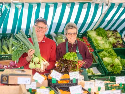zwei Markt Beschicker hinter einem Stand mit Gemüse und Obst