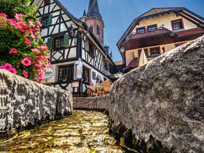 Aus der Perspektive von unten von einem Bächlein blickt man auf die Kirche und ein Fachwerkhaus